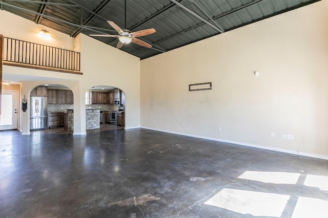 unfurnished living room featuring baseboards, arched walkways, finished concrete floors, and a towering ceiling