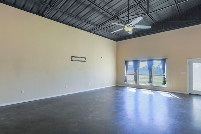 empty room with a towering ceiling, baseboards, concrete flooring, and ceiling fan