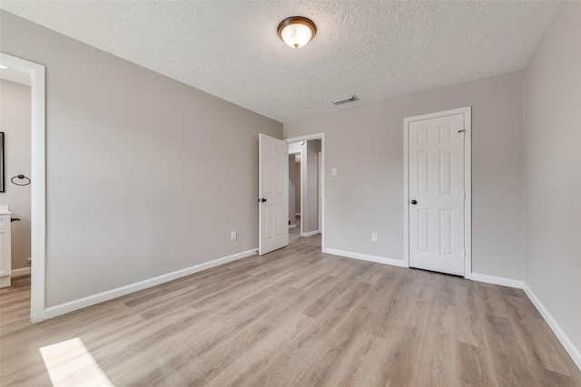 unfurnished bedroom with visible vents, light wood-style flooring, a textured ceiling, and baseboards