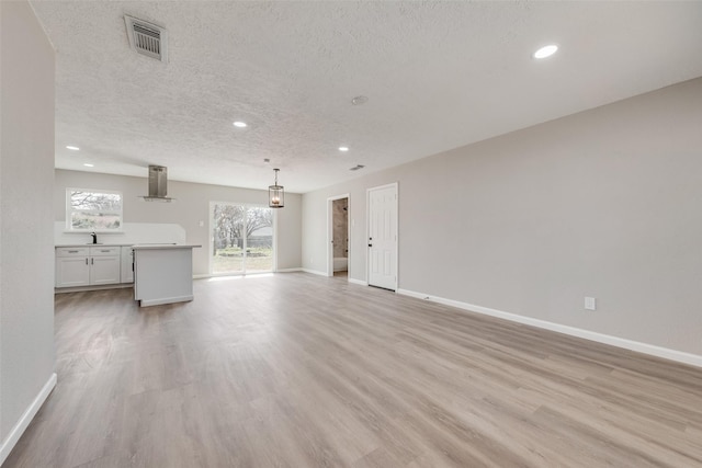 unfurnished living room featuring baseboards, visible vents, recessed lighting, a textured ceiling, and light wood-type flooring