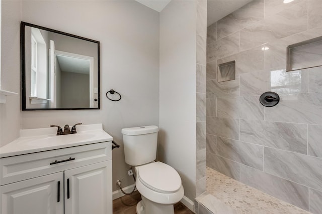 bathroom featuring a tile shower, toilet, vanity, and baseboards