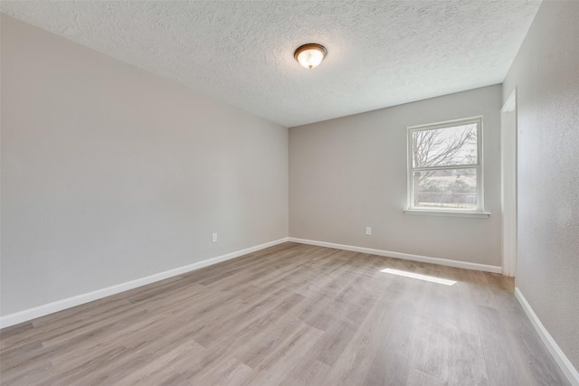 empty room with a textured ceiling, baseboards, and light wood-style floors