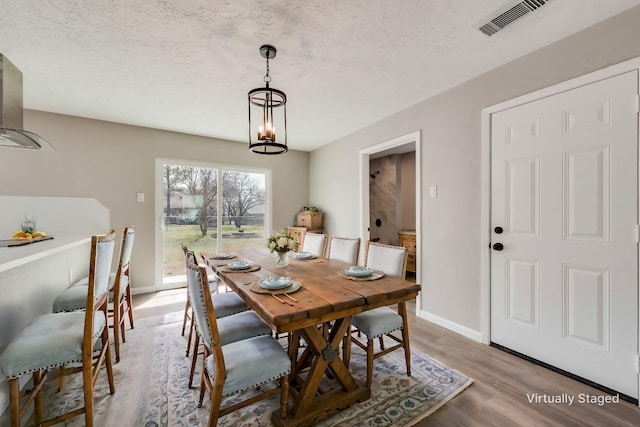 dining space with baseboards, visible vents, light wood finished floors, a textured ceiling, and a notable chandelier