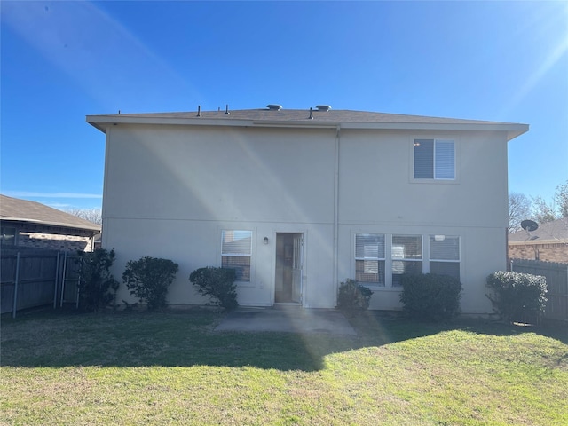 rear view of house featuring stucco siding, a yard, and fence