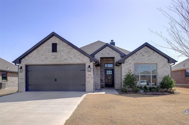 french country home with brick siding, a shingled roof, concrete driveway, a chimney, and a garage