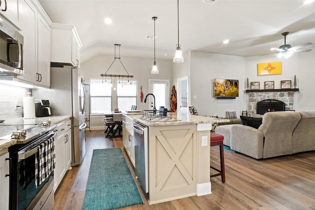 kitchen featuring open floor plan, a breakfast bar, a stone fireplace, wood finished floors, and stainless steel appliances