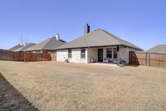 rear view of property with a fenced backyard, a yard, brick siding, a chimney, and a patio area