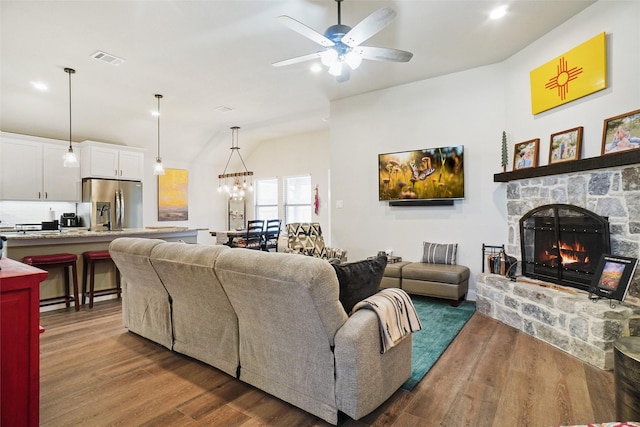 living area with visible vents, ceiling fan with notable chandelier, a fireplace, and wood finished floors