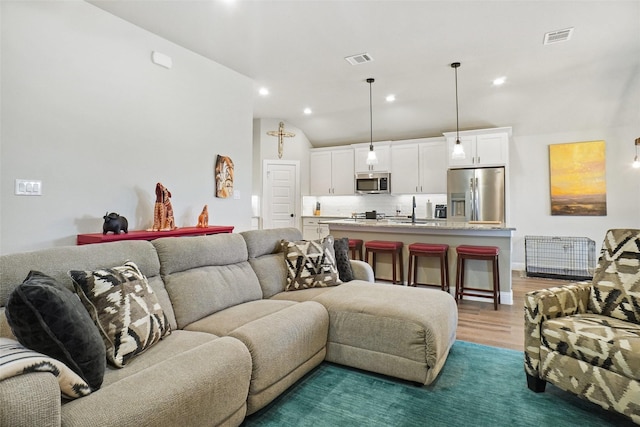 living room featuring recessed lighting, visible vents, vaulted ceiling, and light wood finished floors