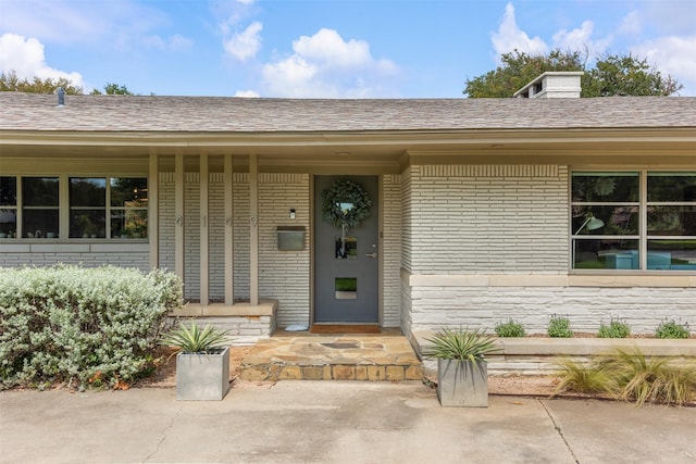 view of exterior entry featuring brick siding and roof with shingles