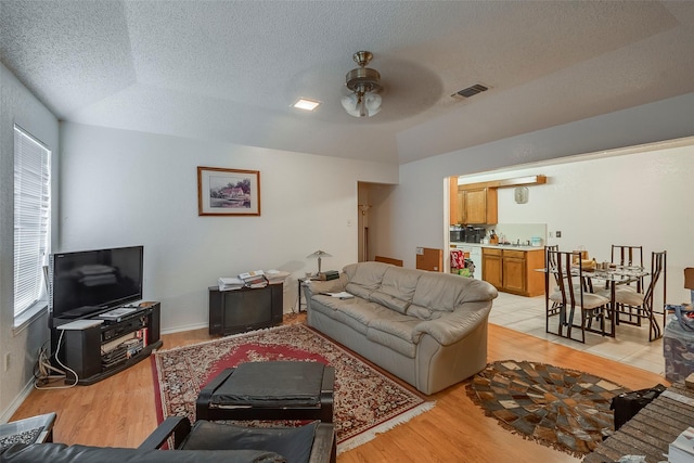 living room featuring light wood-type flooring, visible vents, a ceiling fan, a textured ceiling, and baseboards