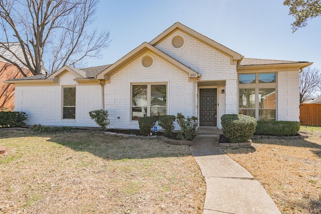view of front facade with brick siding, a front yard, and fence