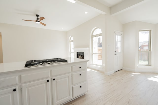 kitchen with lofted ceiling with beams, white cabinetry, stainless steel gas stovetop, light wood finished floors, and a brick fireplace