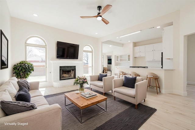 living area with a ceiling fan, a brick fireplace, baseboards, light wood-style floors, and recessed lighting