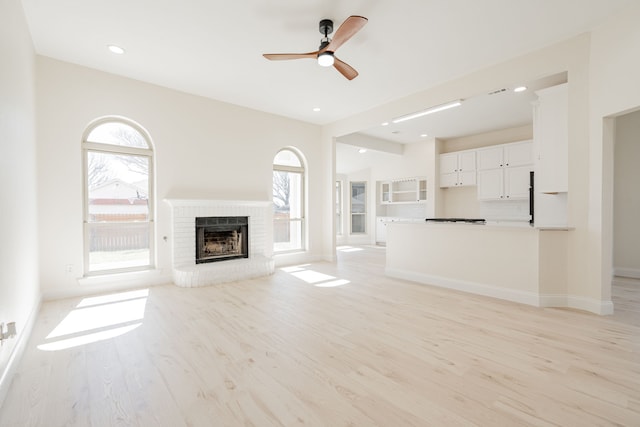 unfurnished living room with light wood-style flooring, a ceiling fan, recessed lighting, baseboards, and a brick fireplace