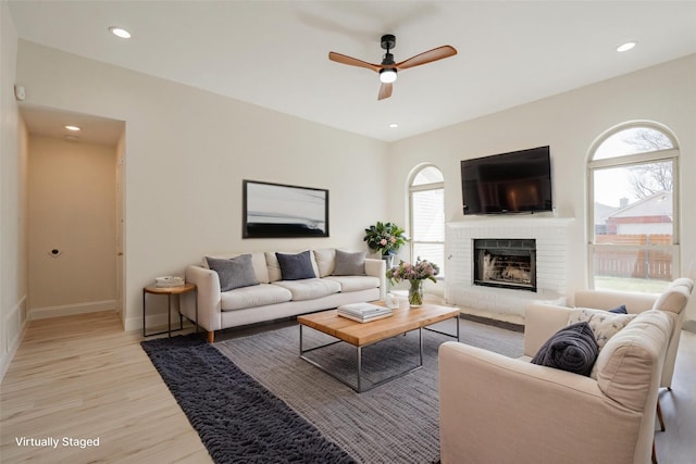 living room featuring a ceiling fan, light wood-style floors, a healthy amount of sunlight, and a fireplace