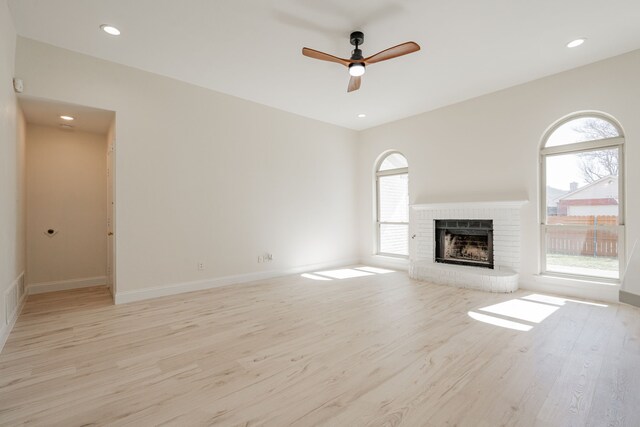 unfurnished living room featuring a ceiling fan, light wood-style floors, a fireplace, and a wealth of natural light