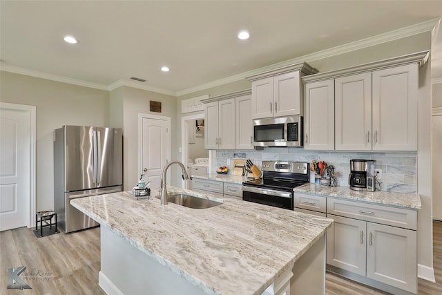 kitchen featuring a center island with sink, a sink, backsplash, light wood-style floors, and appliances with stainless steel finishes