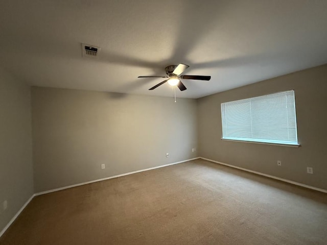 carpeted spare room with visible vents, baseboards, and ceiling fan