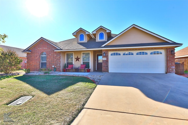 view of front of house with a front yard, driveway, roof with shingles, an attached garage, and brick siding