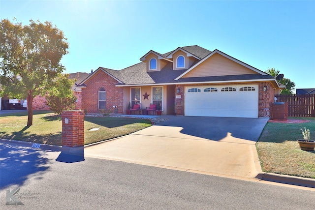 view of front of home with brick siding, fence, a front yard, driveway, and an attached garage