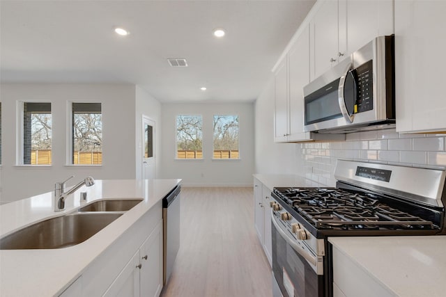 kitchen with a sink, appliances with stainless steel finishes, white cabinets, light countertops, and decorative backsplash