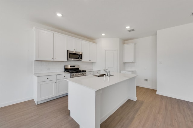 kitchen with light wood finished floors, a center island with sink, stainless steel appliances, and a sink