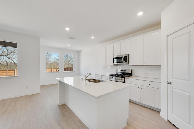 kitchen with an island with sink, a sink, stainless steel appliances, tasteful backsplash, and light wood-type flooring