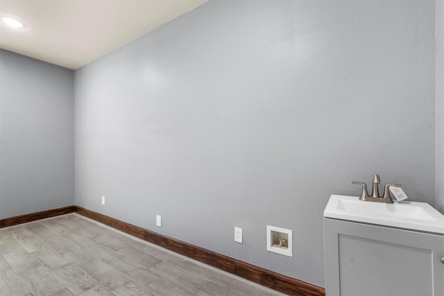 interior space with hookup for a washing machine, baseboards, laundry area, a sink, and light wood-type flooring