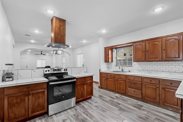 kitchen featuring light countertops, stainless steel range with electric stovetop, backsplash, and a sink