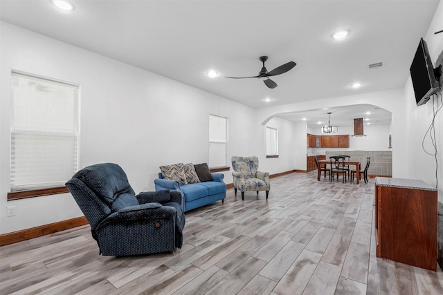 living room featuring visible vents, light wood finished floors, baseboards, arched walkways, and ceiling fan with notable chandelier