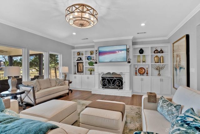 living area with visible vents, a brick fireplace, wood finished floors, and crown molding