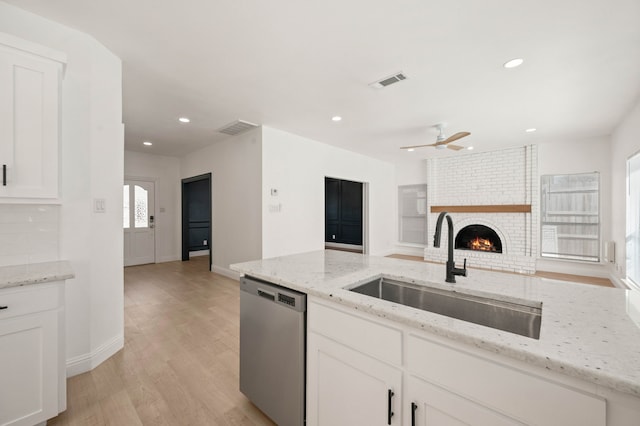 kitchen featuring visible vents, white cabinetry, a fireplace, a sink, and dishwasher