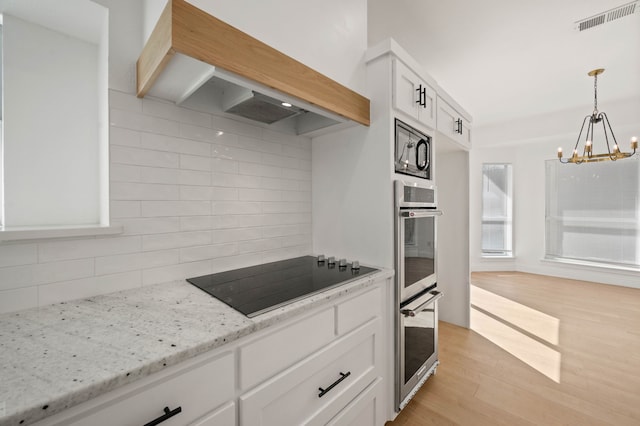 kitchen with light wood finished floors, visible vents, black appliances, custom range hood, and white cabinetry