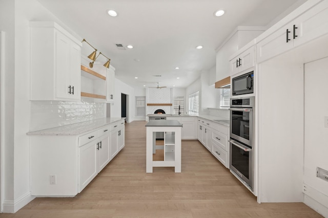 kitchen featuring light wood-style flooring, open shelves, a peninsula, black microwave, and decorative backsplash