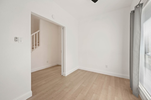 spare room featuring baseboards, light wood-style floors, and stairs