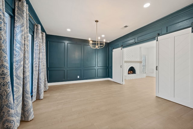 interior space featuring a barn door, a decorative wall, an inviting chandelier, light wood finished floors, and a brick fireplace