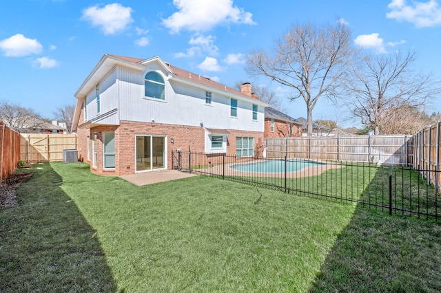 rear view of property featuring a fenced backyard, a yard, brick siding, a chimney, and a patio area