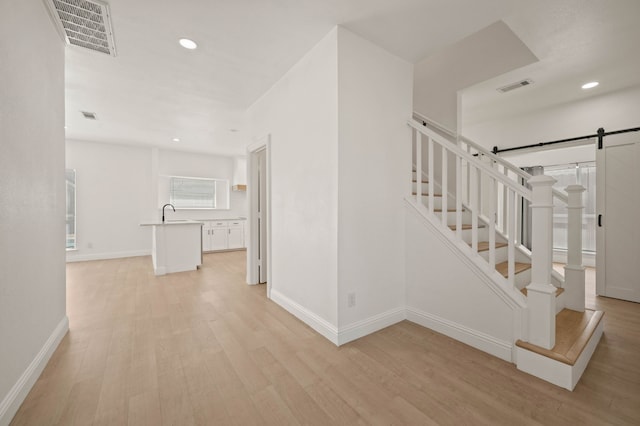 hall with a barn door, light wood-style flooring, stairway, and visible vents