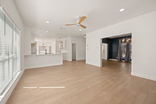 unfurnished living room with light wood finished floors, recessed lighting, ceiling fan with notable chandelier, and baseboards