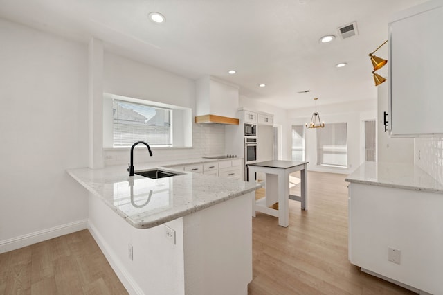 kitchen featuring a sink, backsplash, stainless steel oven, and light wood finished floors