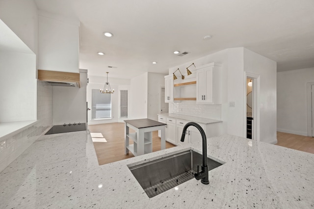 kitchen featuring a sink, open shelves, backsplash, white cabinetry, and light stone countertops