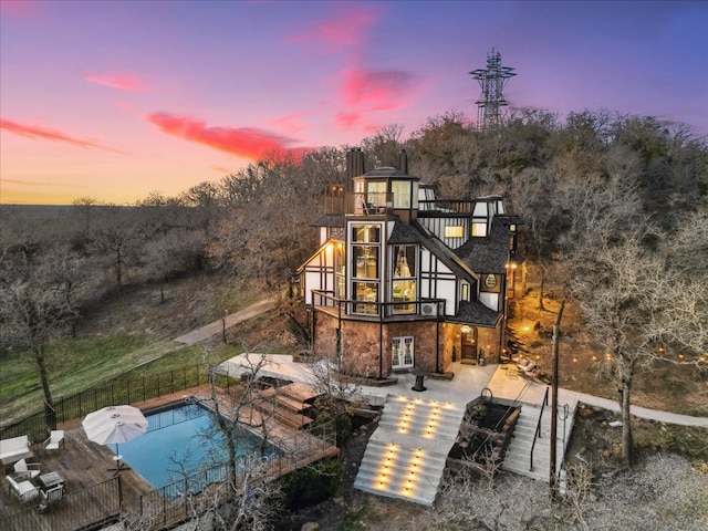 back of house at dusk with a patio, fence, a fenced in pool, french doors, and stone siding