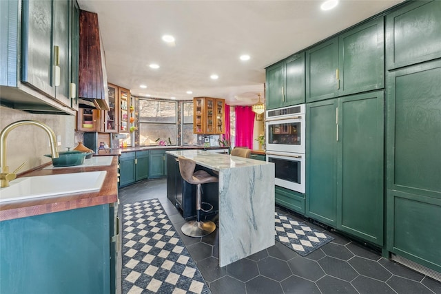 kitchen with glass insert cabinets, green cabinetry, a sink, recessed lighting, and double oven