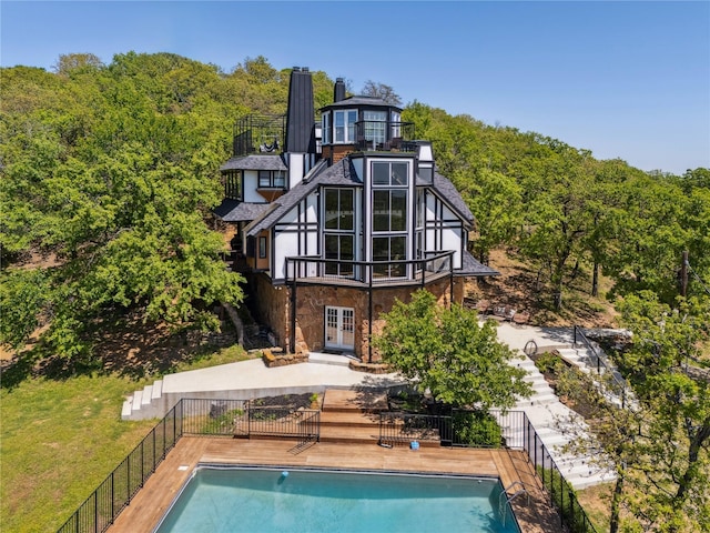 back of property with french doors, a view of trees, a fenced in pool, and stone siding
