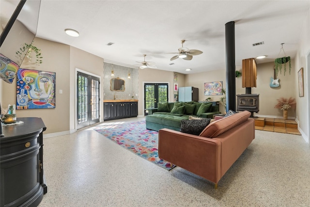 living room featuring baseboards, a wood stove, a ceiling fan, speckled floor, and french doors