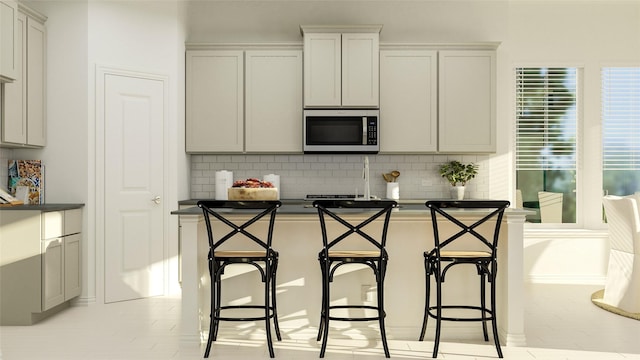 kitchen with dark countertops, stainless steel microwave, a breakfast bar, and decorative backsplash