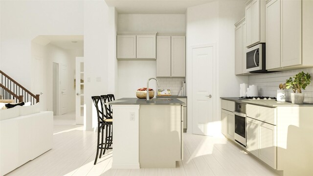 kitchen featuring dark countertops, an island with sink, decorative backsplash, stainless steel appliances, and a sink