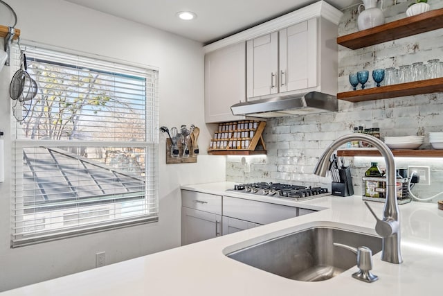 kitchen with tasteful backsplash, a sink, under cabinet range hood, light countertops, and open shelves