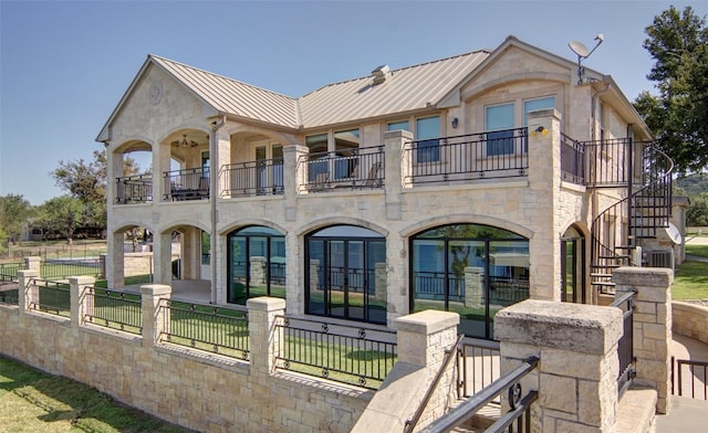 view of front of house with a front lawn, a standing seam roof, a fenced front yard, metal roof, and a balcony